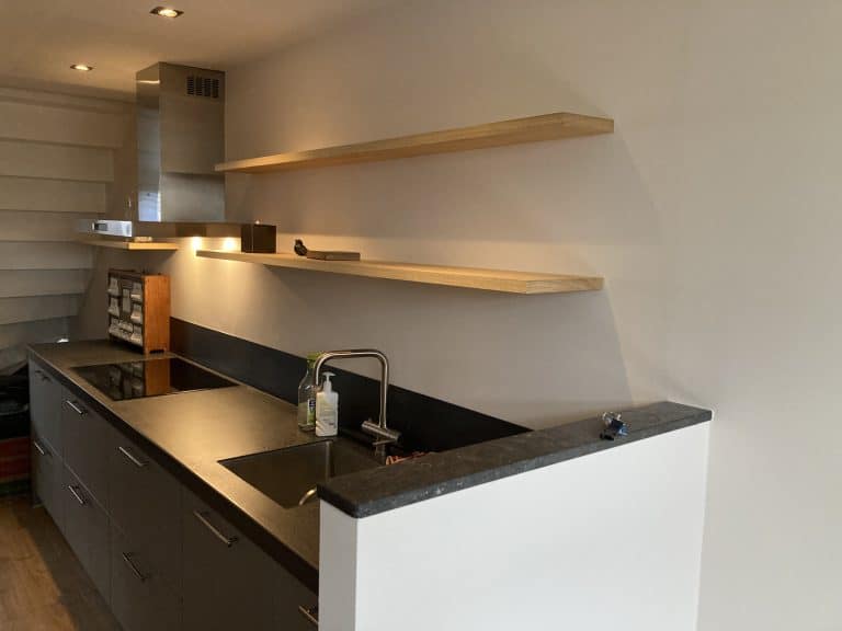 Twee zwevende wandplanken van abachi op maat boven een grijze keuken met spots, Abcoude — Senders Meubelmakerij